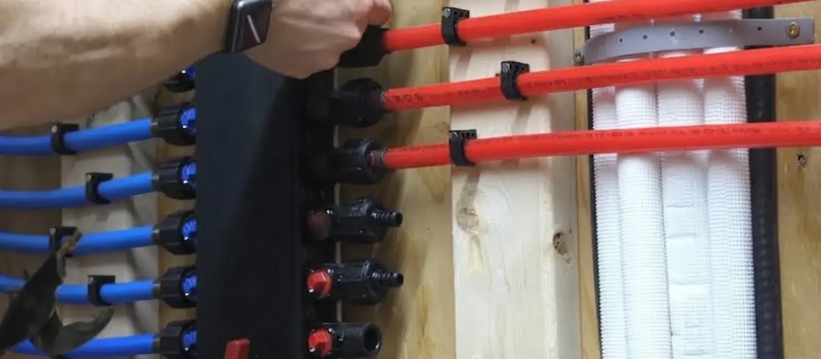 Hand holds red and blue PEX tubes connected to a black plumbing manifold