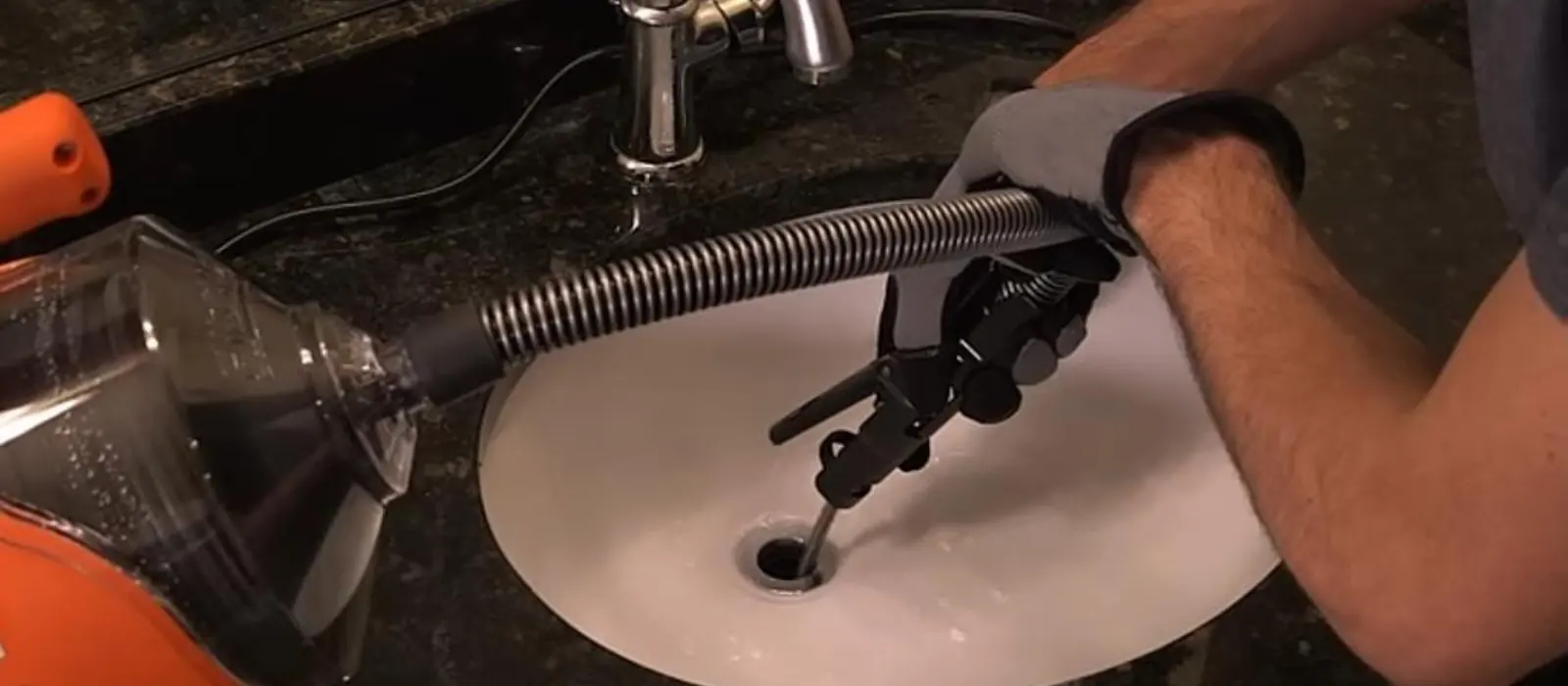 Gloved hand feeds a drain auger cable into a bathroom sink drain